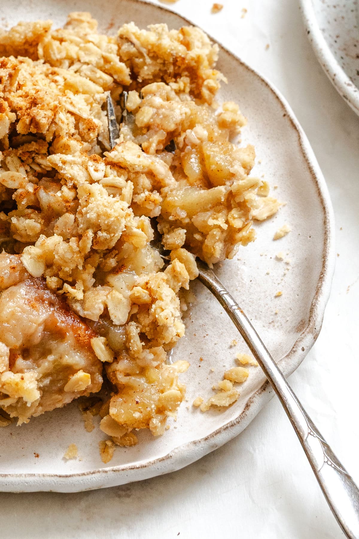 A fork taking a bite of apple crisp on a cream plate. 