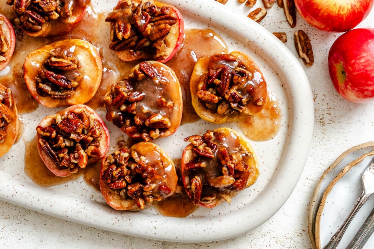 Baked apples on a platter next to fresh apples.