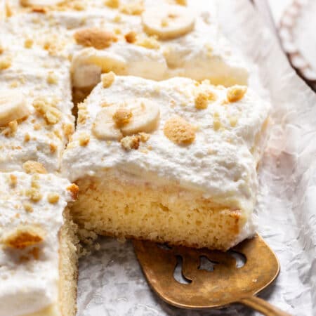 A cake server removing a slice of banana pudding poke cake from the cake.