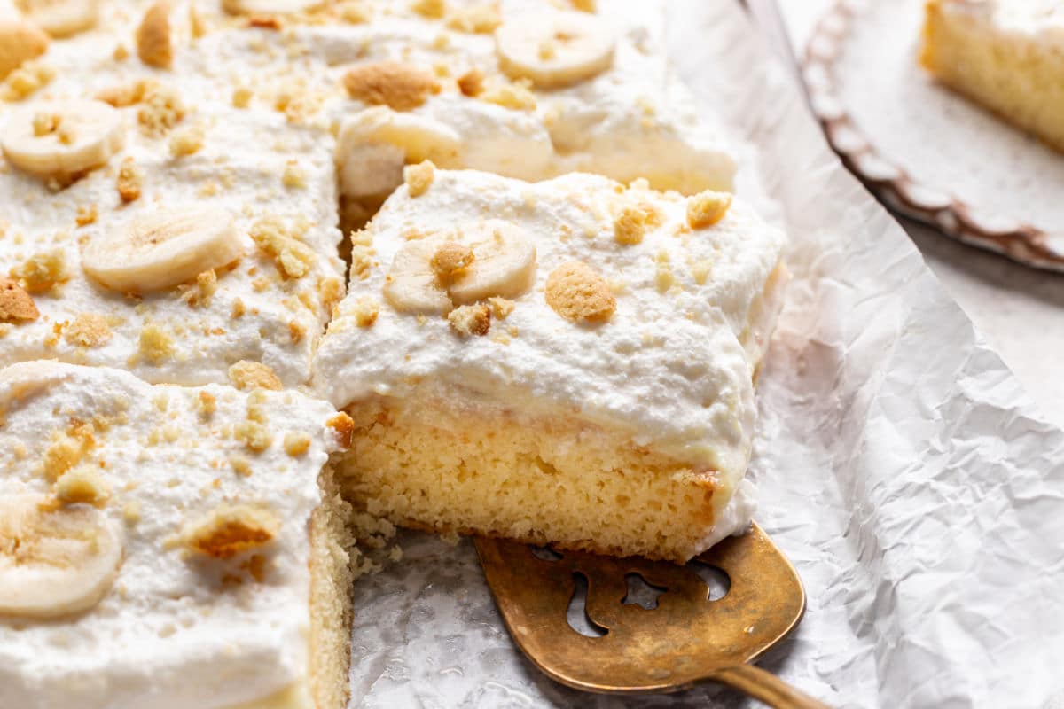 A cake server removing a slice of banana pudding poke cake from the cake.