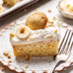A slice of banana pudding poke cake topped with a slice of banana and a nilla wafer.