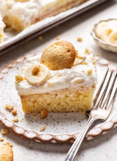 A slice of banana pudding poke cake topped with a slice of banana and a nilla wafer.