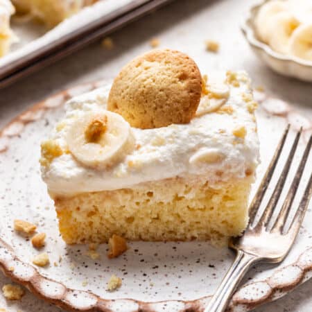 A slice of banana pudding poke cake topped with a slice of banana and a nilla wafer.