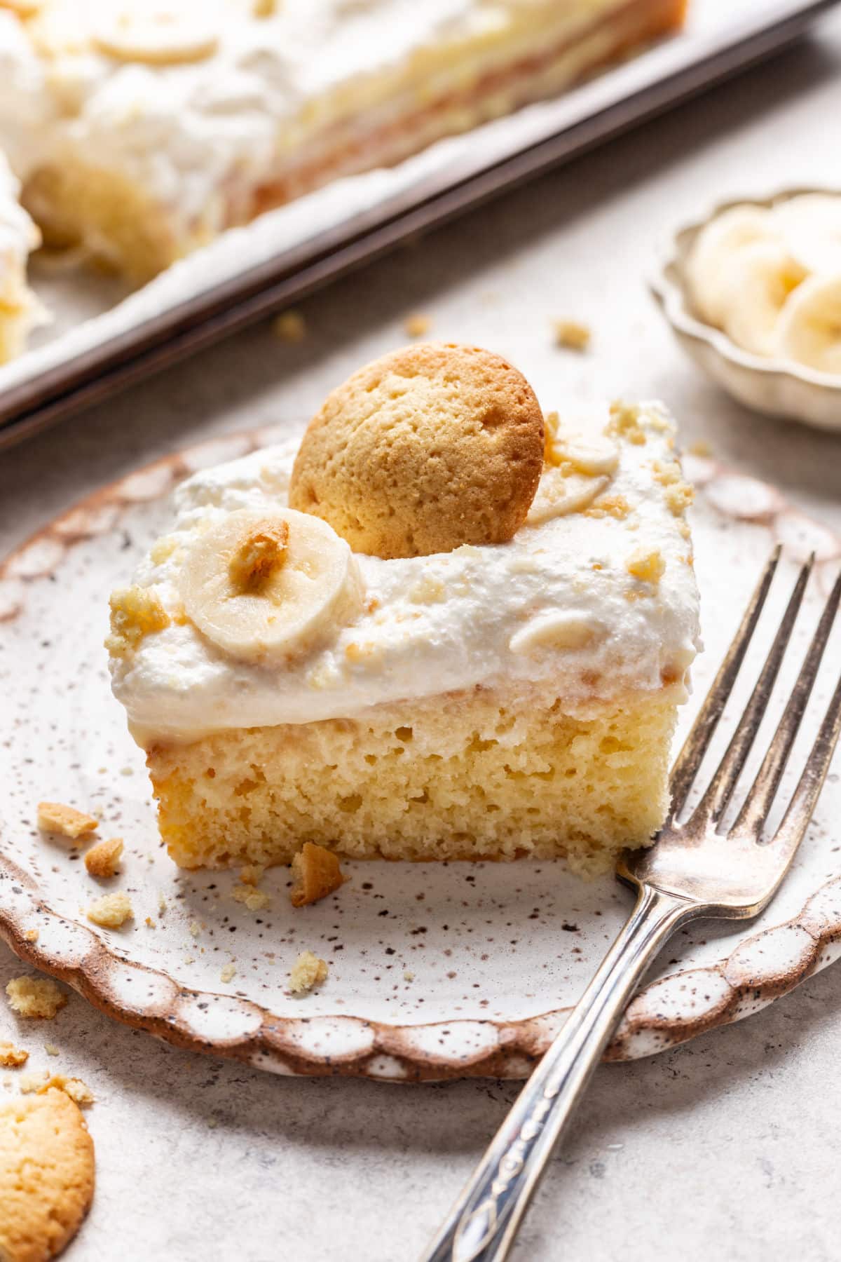 A slice of banana pudding poke cake topped with a slice of banana and a nilla wafer.