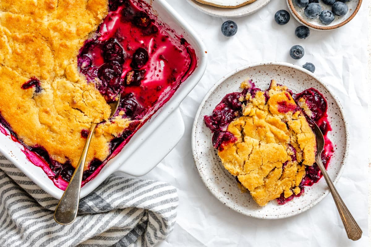 A plate of blueberry cobbler next to the dish of cobbler.