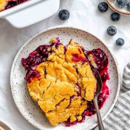 A plate of blueberry cobbler next to a dish of blueberries.