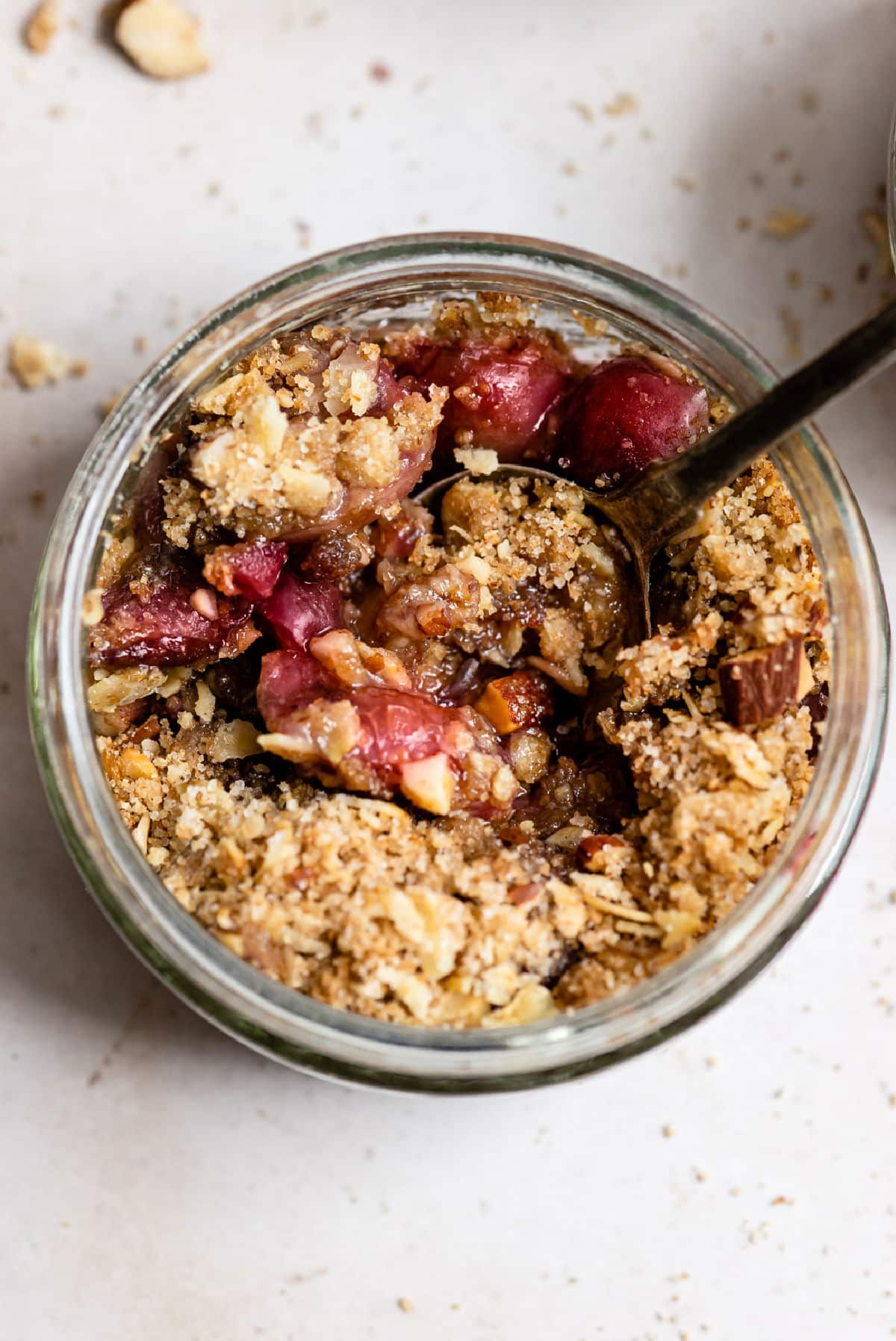 A ramekin on cherry crisp with a black spoon in it.