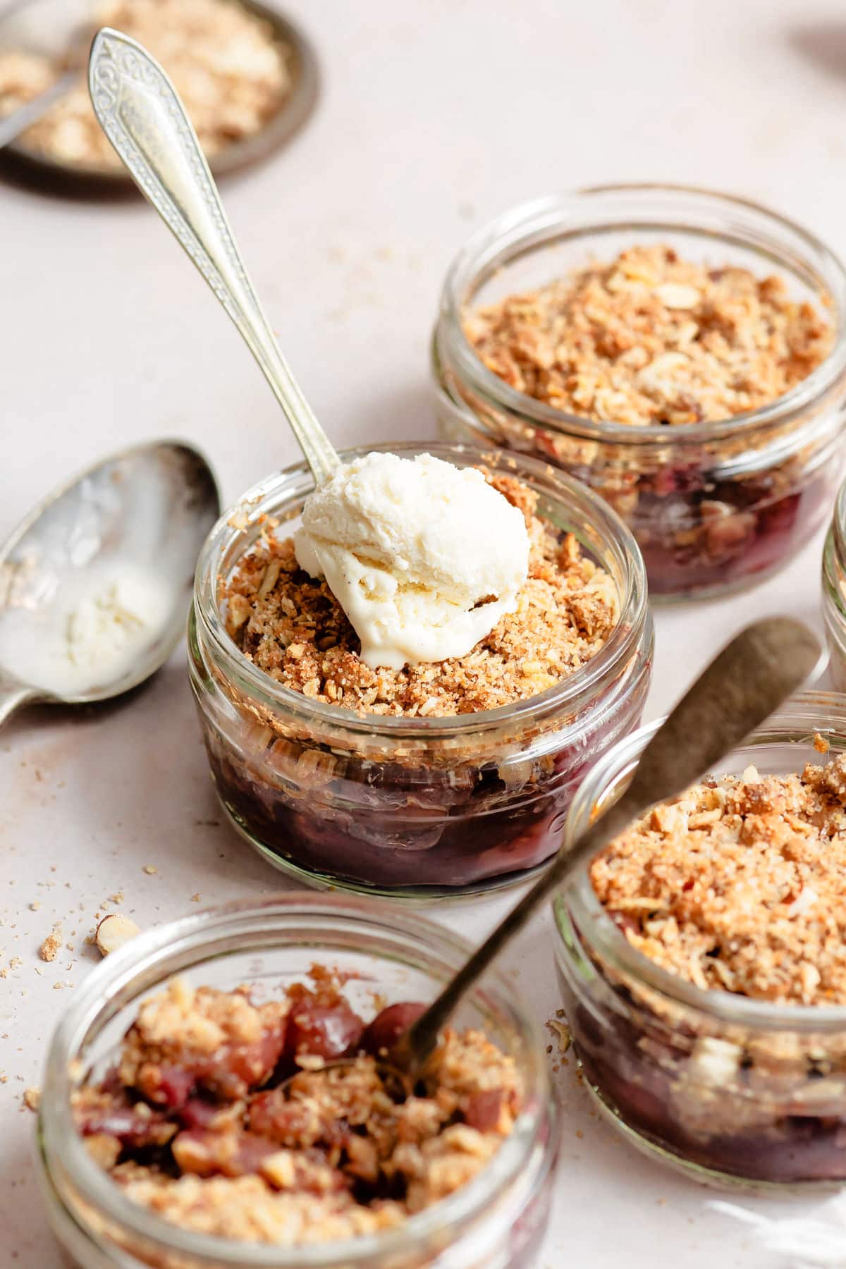 A ramekin of cherry crisp with vanilla ice cream surrounded by more ramekins of cherry crisp. 