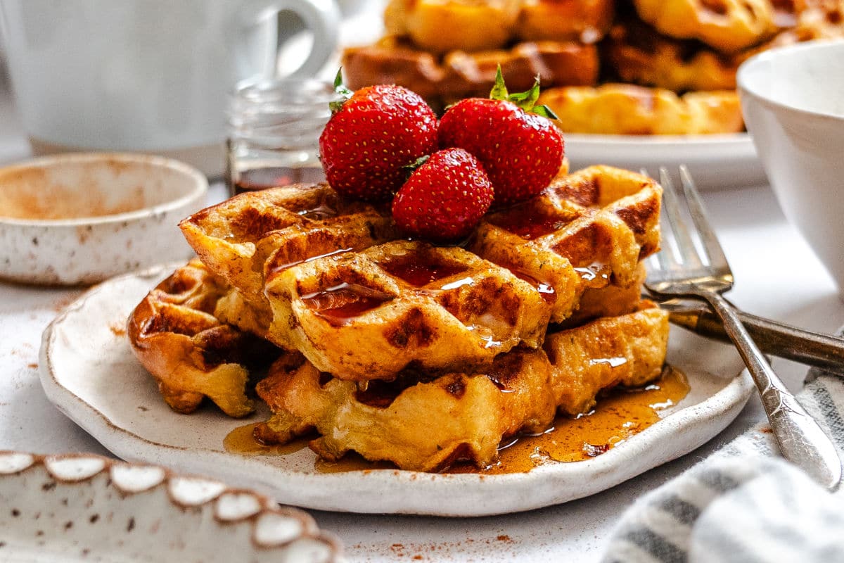 Two French toast waffles on a plate next to a fork and a dish of cinnamon.