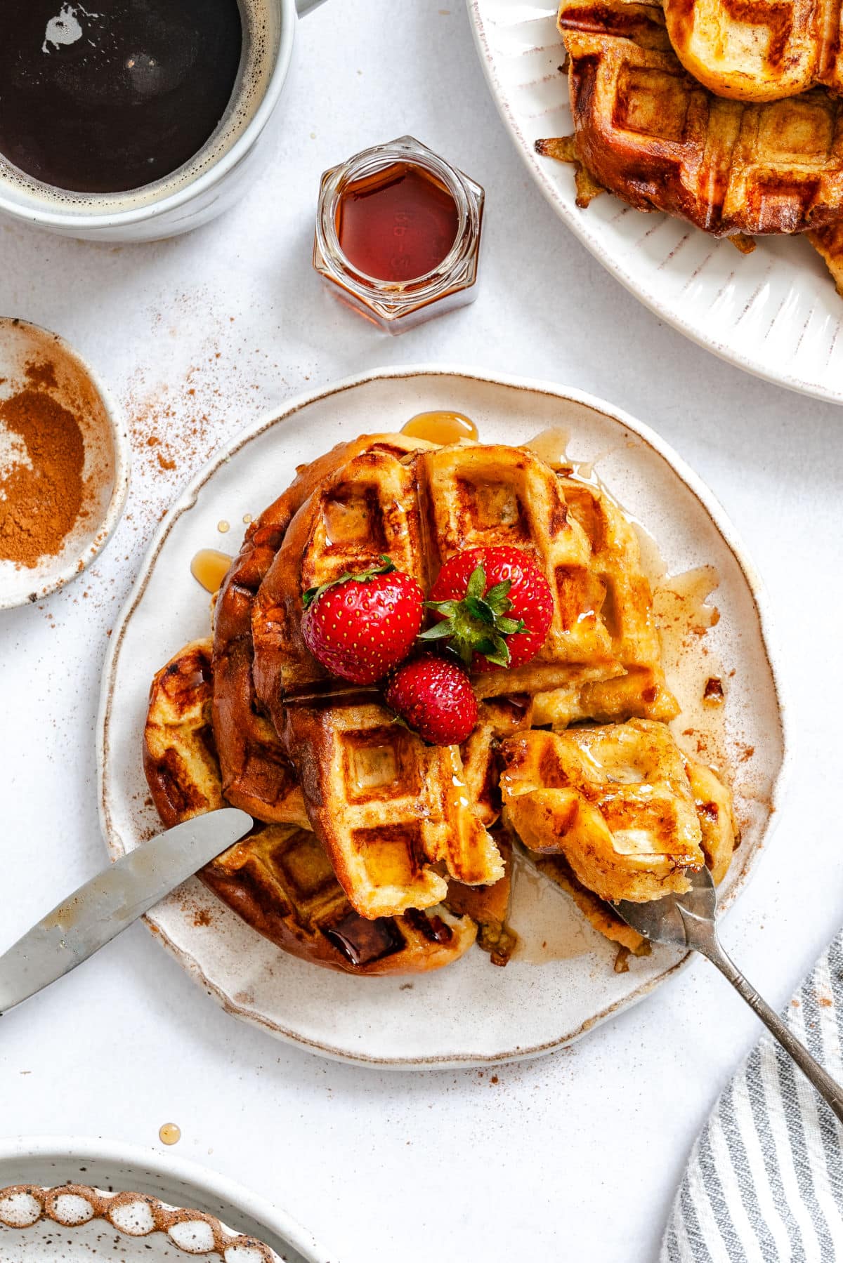 A fork and knife taking a bite of a French toast waffle on a plate.