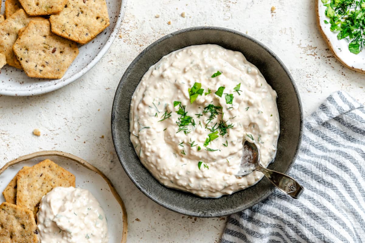 A dish of cottage cheese herb dip next to a plate of whole grain crackers. 