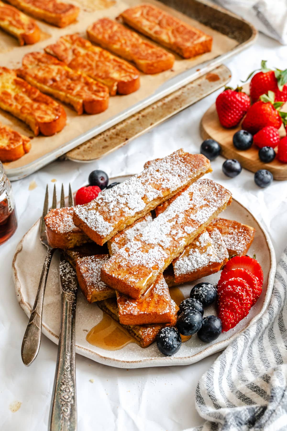 Une assiette de bâtonnets de pain perdu saupoudrés de sucre en poudre et de baies.
