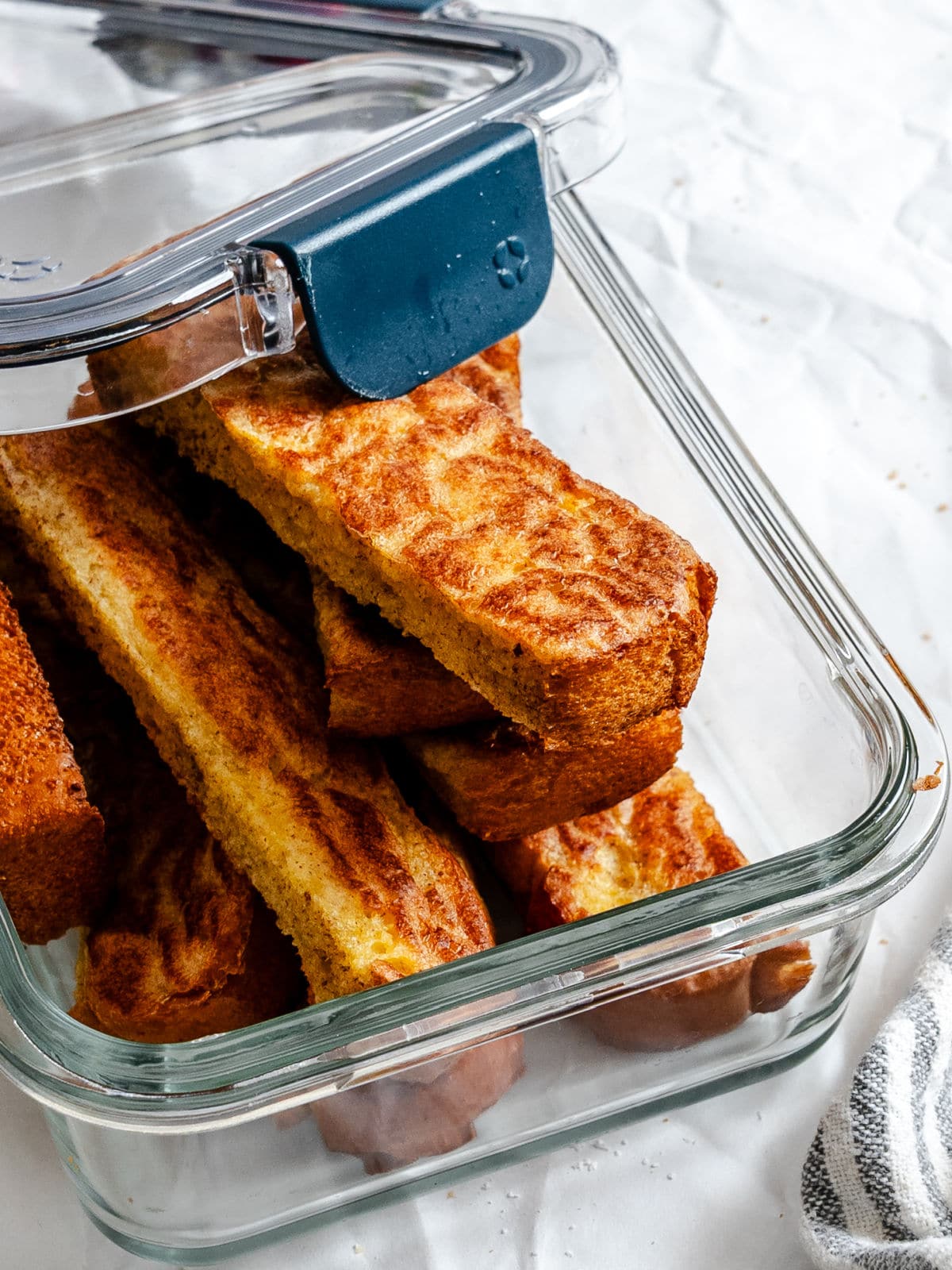 French toast sticks in a partially open glass storage container. 