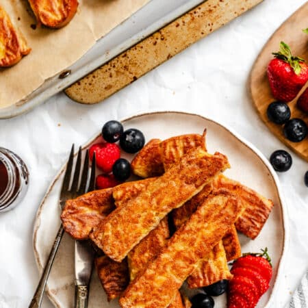 A plate of French toast sticks next to the pan of sticks.