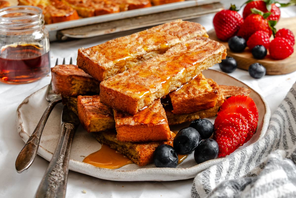 Une assiette de bâtonnets de pain perdu garnis de sirop et de baies.