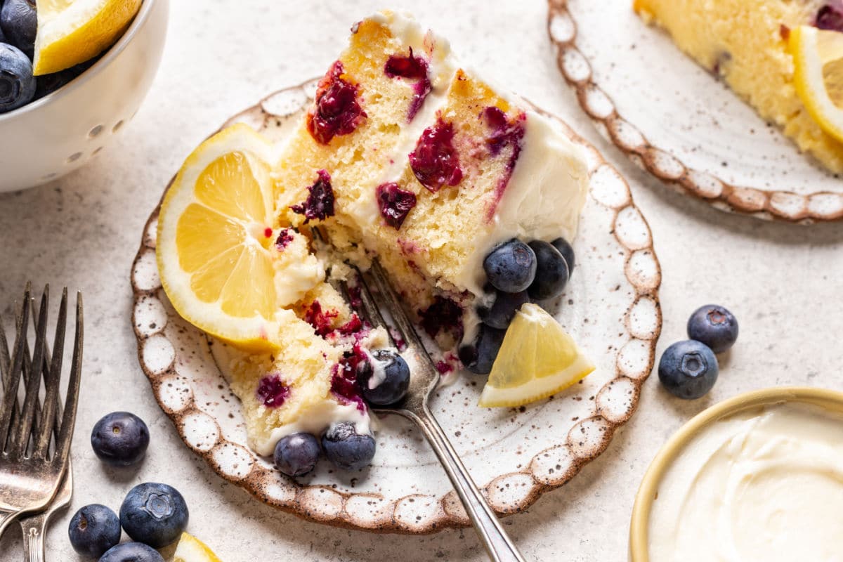 A fork taking a bite of a slice of lemon blueberry cake.