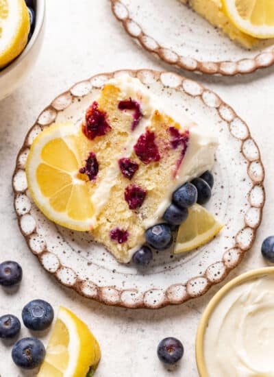 A slice of lemon blueberry cake with a piece of lemon on the plate.
