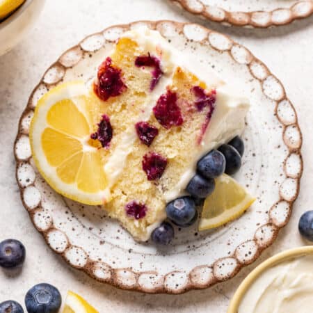 A slice of lemon blueberry cake with a piece of lemon on the plate.
