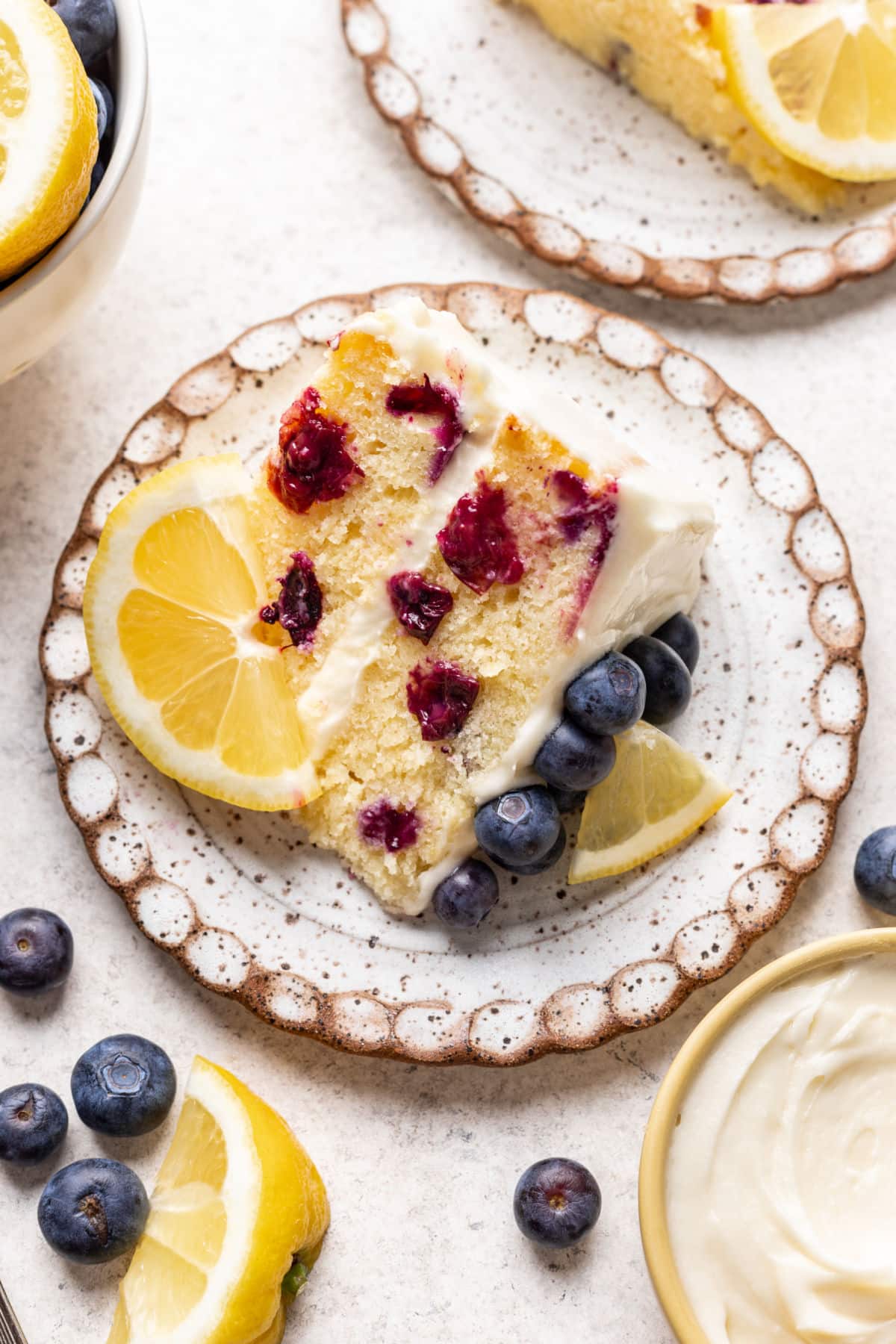 A slice of lemon blueberry cake with a piece of lemon on the plate.