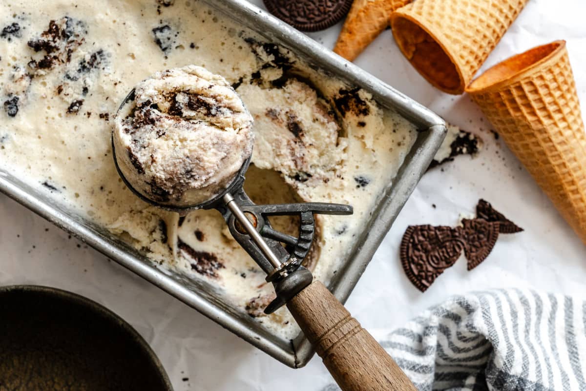 A wood handled ice cream scoop holding a scoop of no churn cookies and cream ice cream.