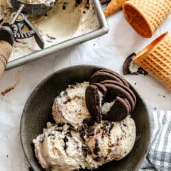 A bowl with three scoops of no churn cookies and cream ice cream in a dish next to the pan of ice cream.