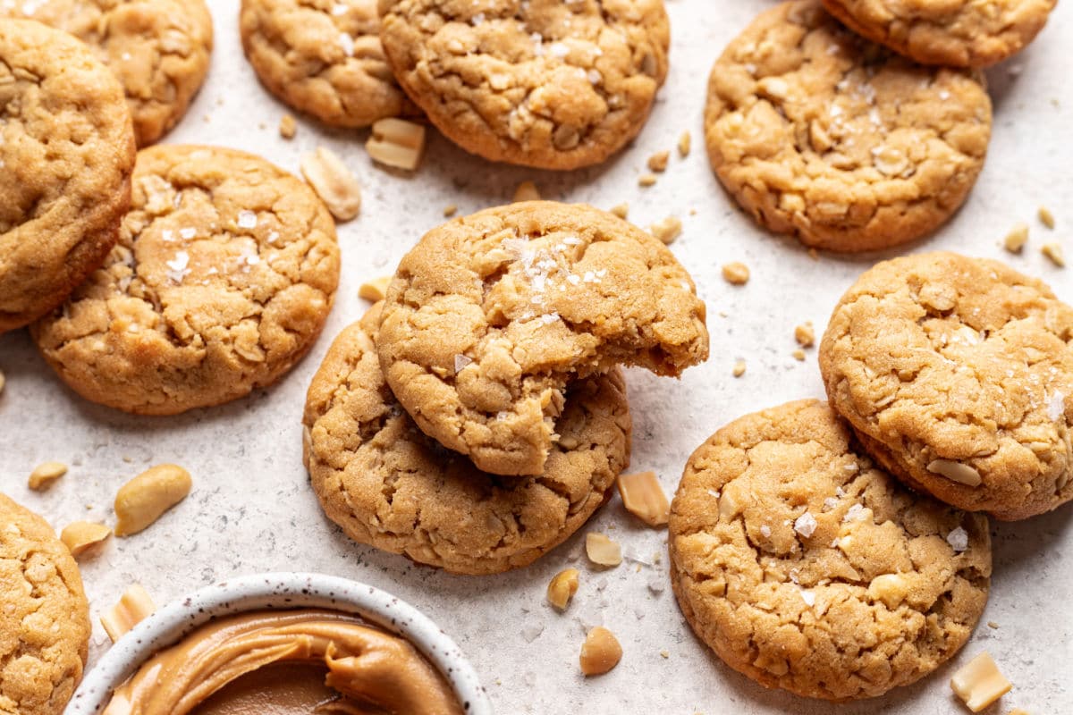 A peanut butter oatmeal cookie with a bite missing on top of another cookie surrounded by overlapping cookies. 