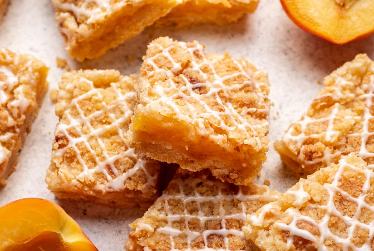 Peach crumb bars - I eat the heart Two peach bars of bars tend against each other surrounded by bars and fresh peaches.