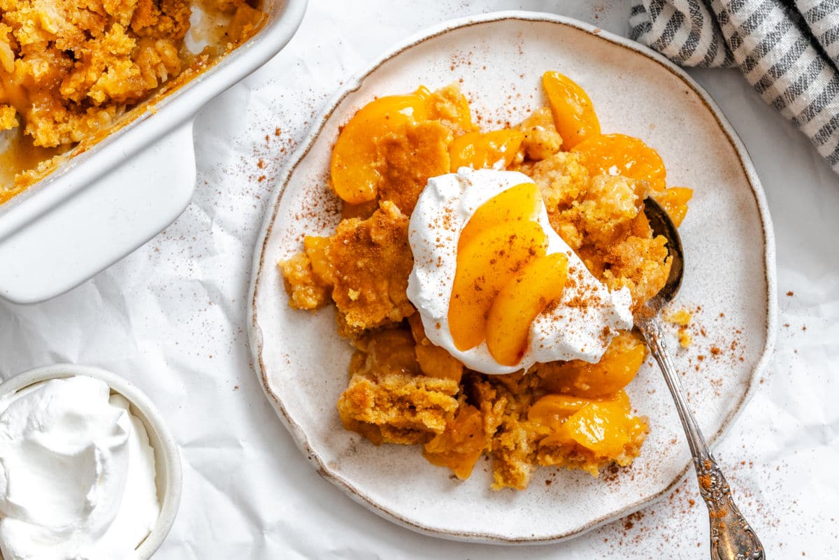 A plate of peach dump cake next to the pan and a striped dish cloth.