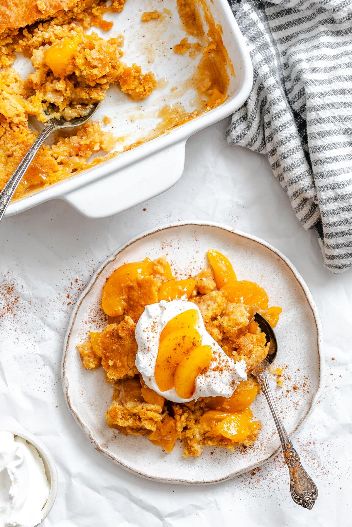 A plate of peach dump cake topped with whipped cream and two peach slices.