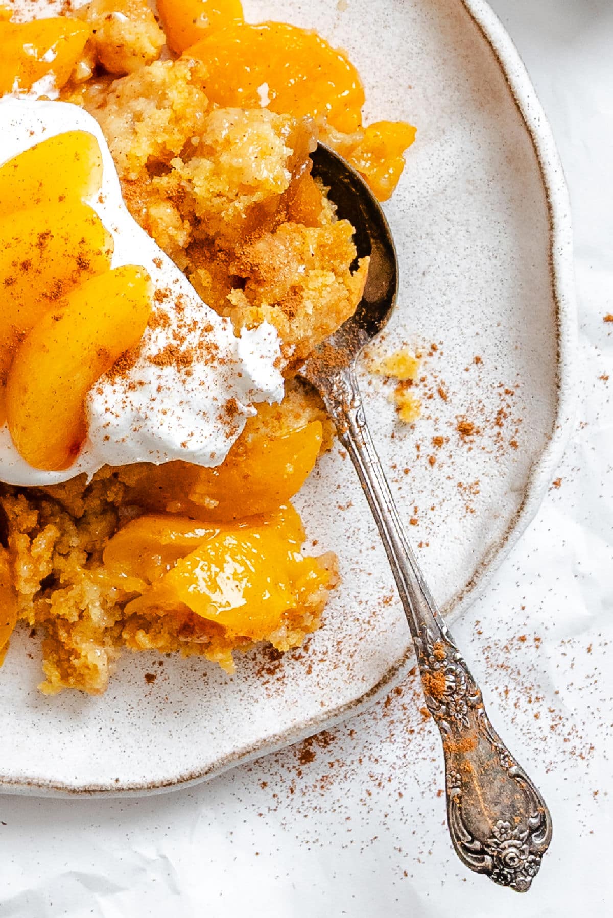 A plate of peach dump cake with a vintage silver spoon in it.