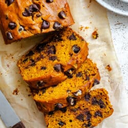 Three slices of pumpkin chocolate chip bread next to the loaf.