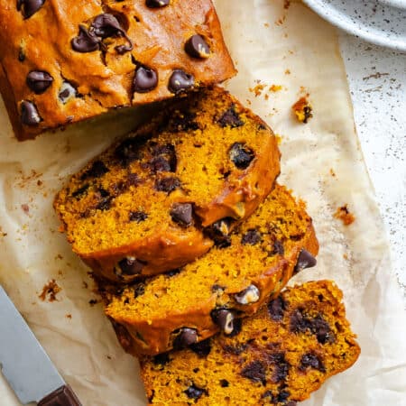 Three slices of pumpkin chocolate chip bread next to the loaf.