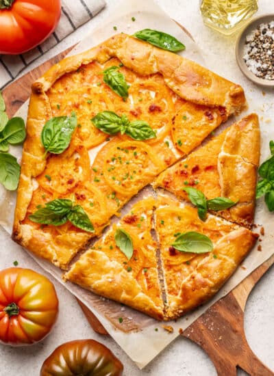 A tomato galette with three slices cut surrounded by fresh heirloom tomatoes.