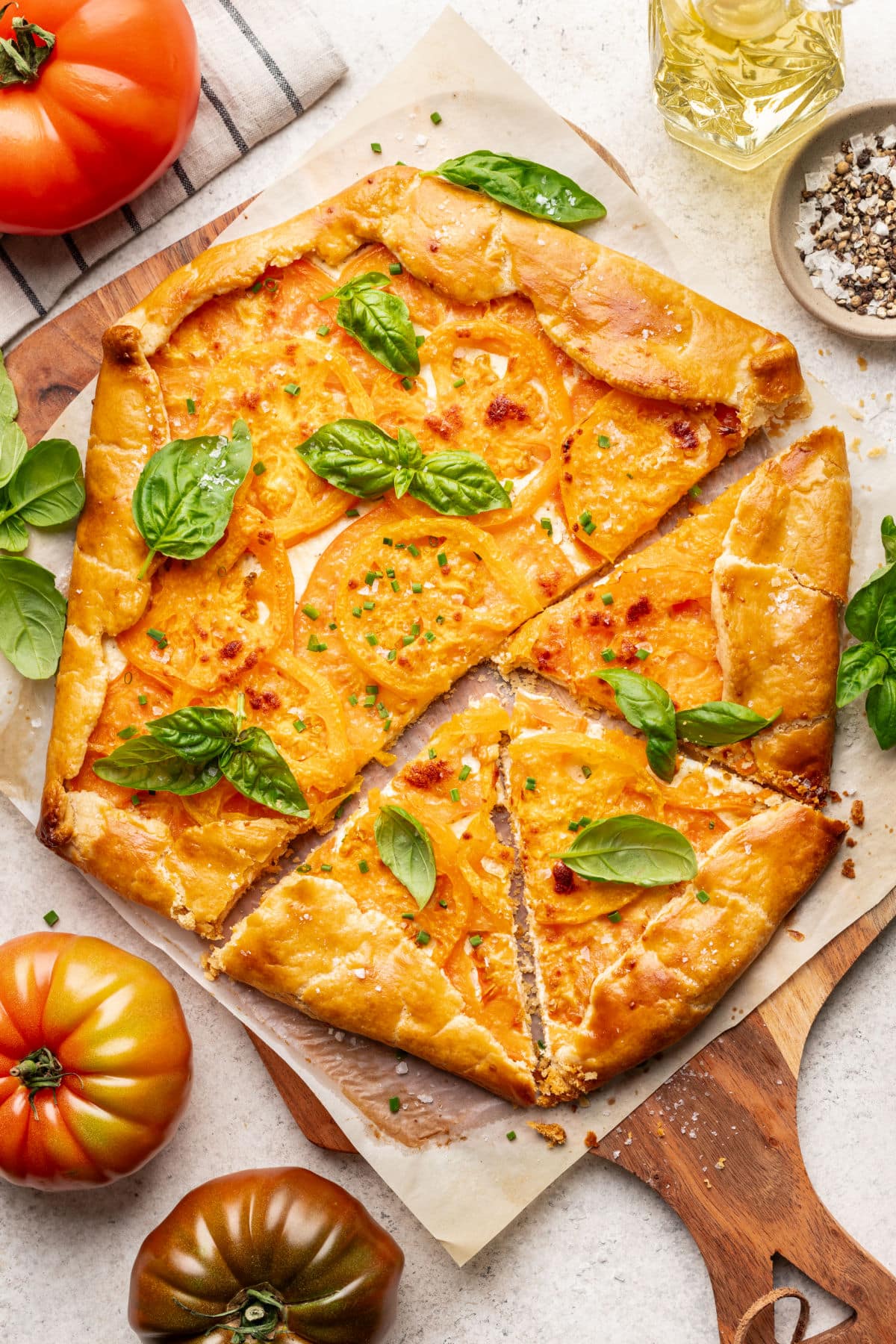 A tomato galette with three slices cut surrounded by fresh heirloom tomatoes.