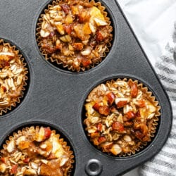 Baked apple crisp oatmeal in a muffin tin next to a kitchen linen.