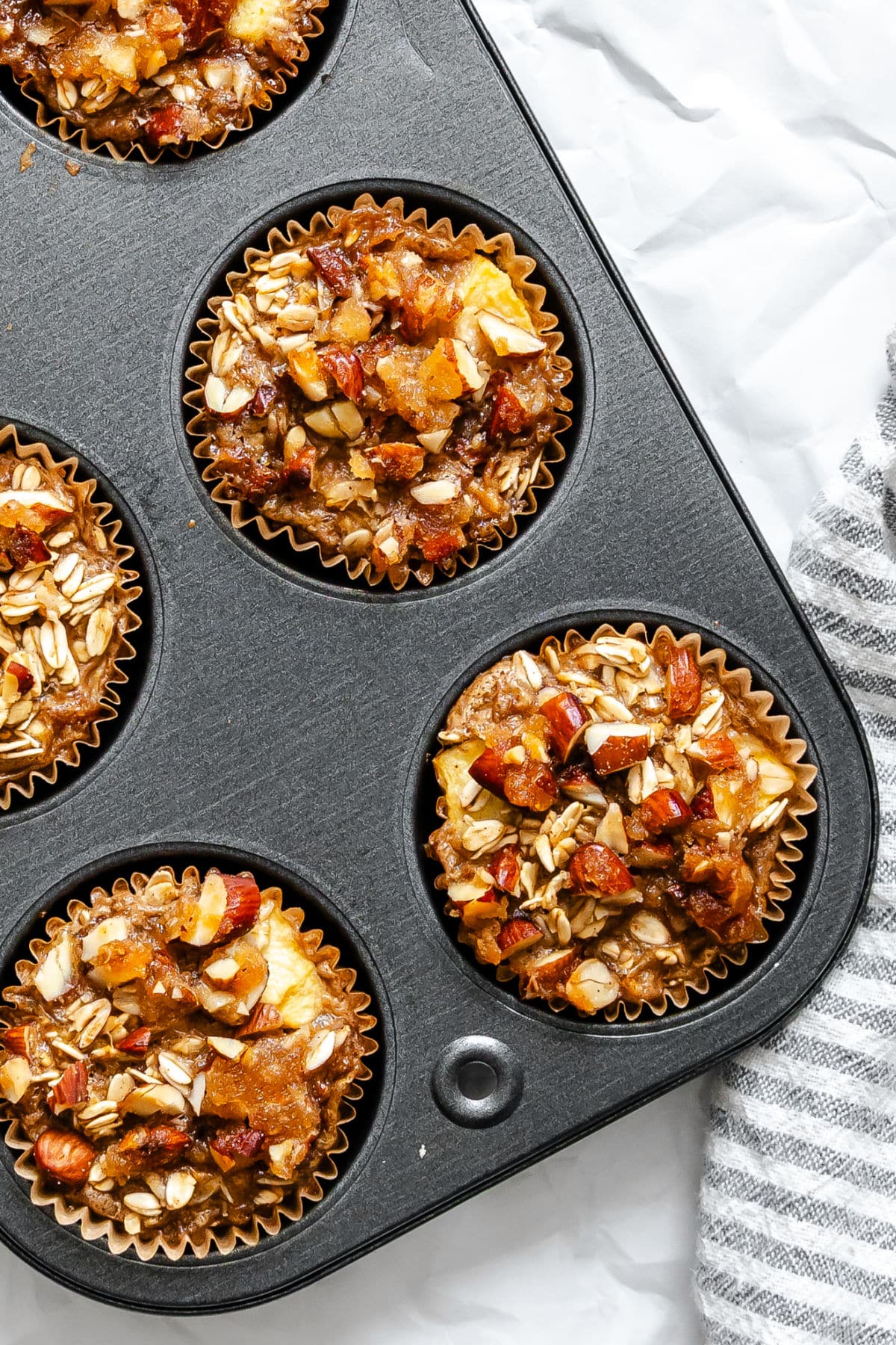 Individual Apple Crisp Oatmeal Baked apple crisp oatmeal in a muffin tin next to a kitchen linen.