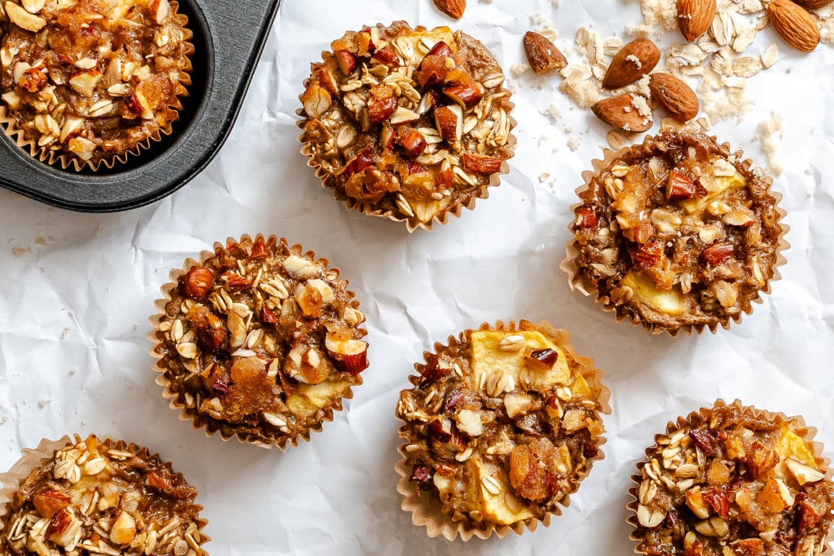 Baked apple crisp oatmeal in cups on a piece of white parchment paper.