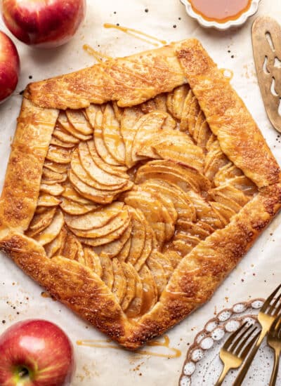 Apple galette drizzled with caramel sauce next to fresh apples.