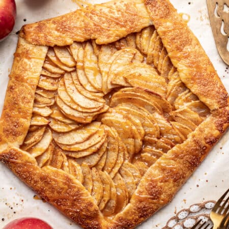 Apple galette drizzled with caramel sauce next to fresh apples.