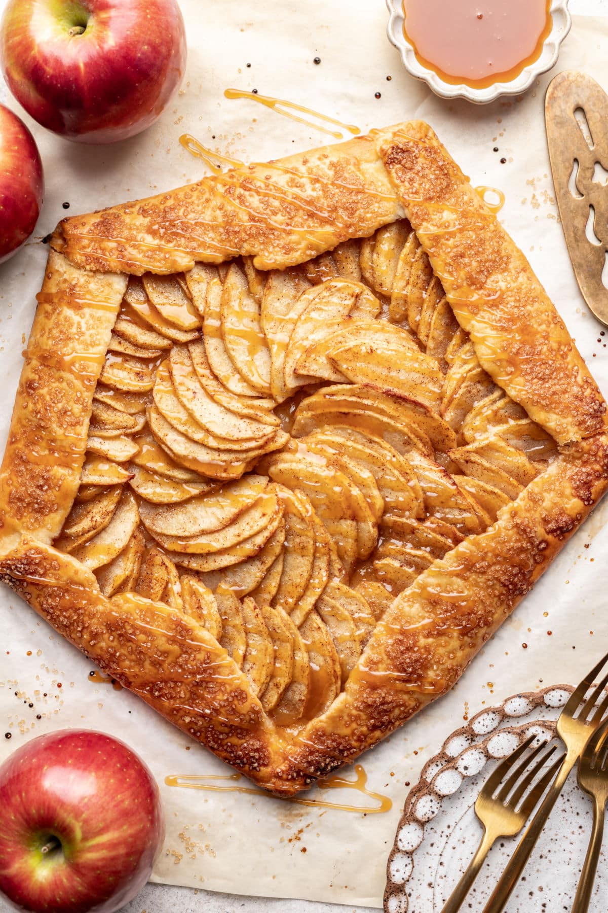 Apple galette drizzled with caramel sauce next to fresh apples.