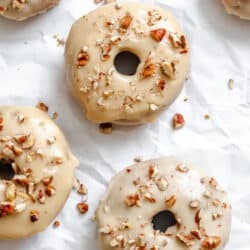 Baked and frosted sweet potato donuts on a piece of white parchment paper.