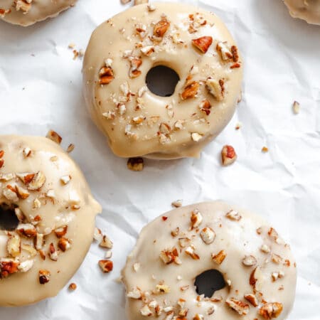 Baked and frosted sweet potato donuts on a piece of white parchment paper.