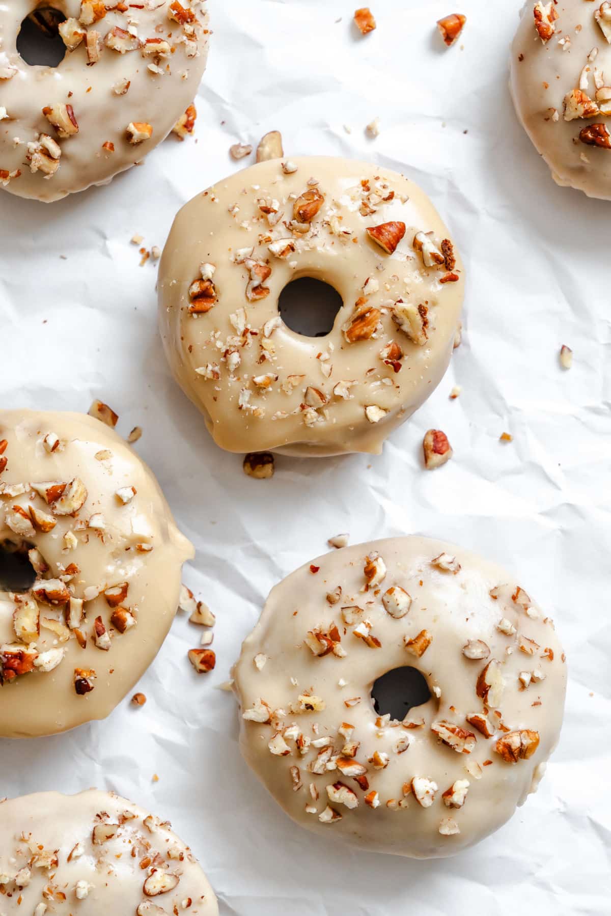 Baked and frosted sweet potato donuts on a piece of white parchment paper.