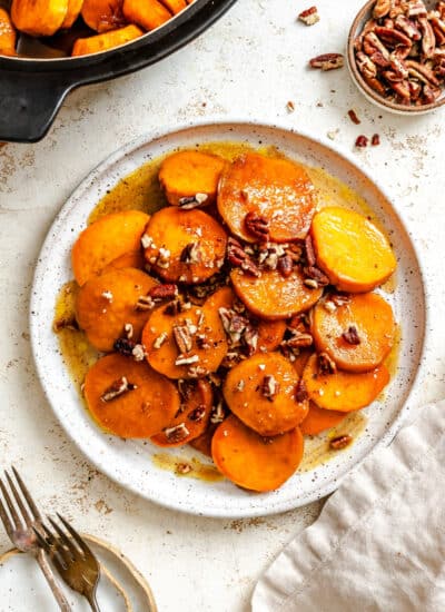 A plate of candied sweet potatoes on a plate next to the pot of sweet potatoes.