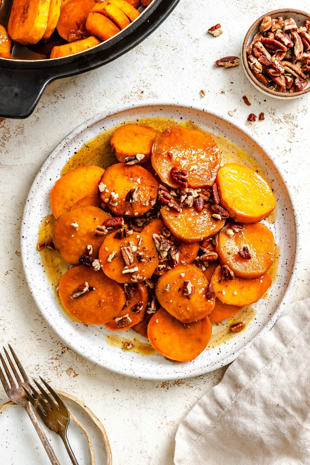 A plate of candied sweet potatoes on a plate next to the pot of sweet potatoes.
