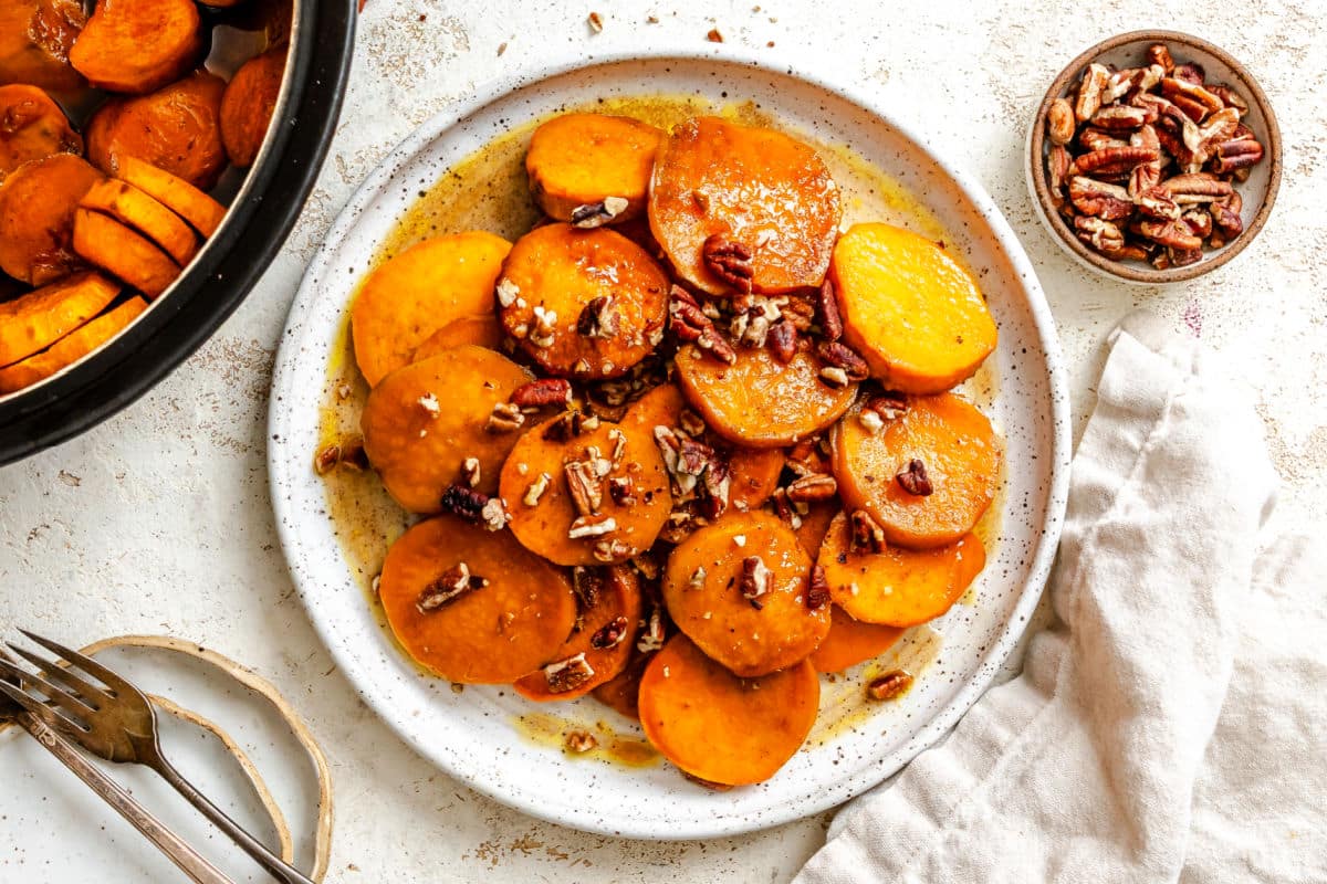 A plate of candied sweet potatoes next to a small dish of pecans.