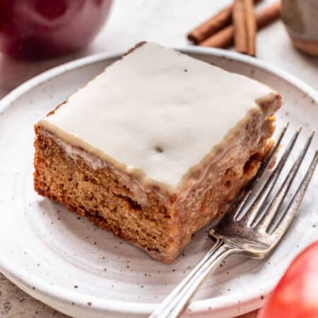 A slice of caramel apple sheet cake on a plate next to apples and cinnamon sticks.