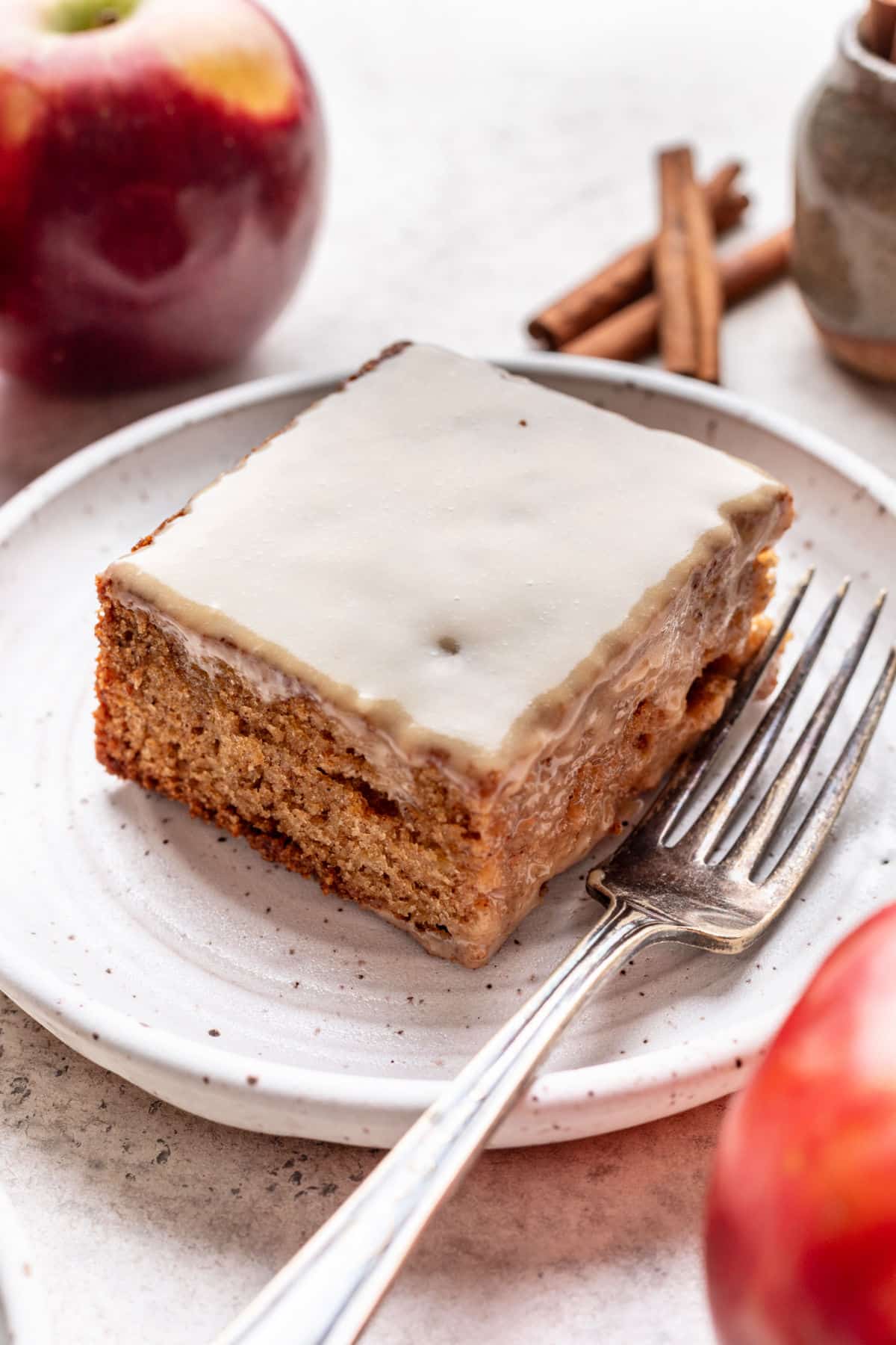 A slice of caramel apple sheet cake on a plate next to apples and cinnamon sticks.