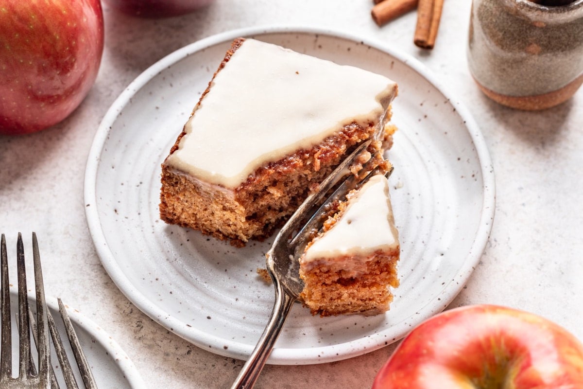 A fork taking a bite of caramel apple sheet cake on a plate.