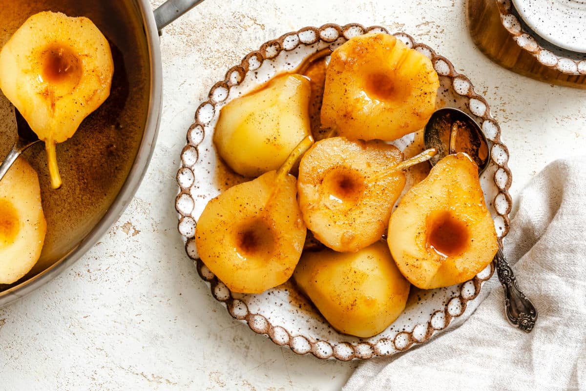 A plate of poached pears next to a pan with pears in it. 